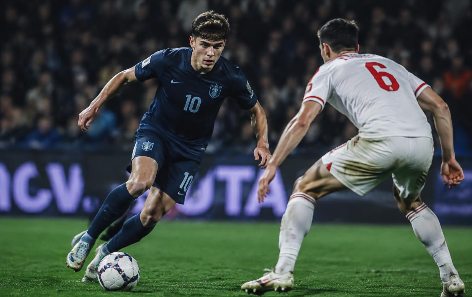 Evan Mitchell dribbling at a defender during a night match
